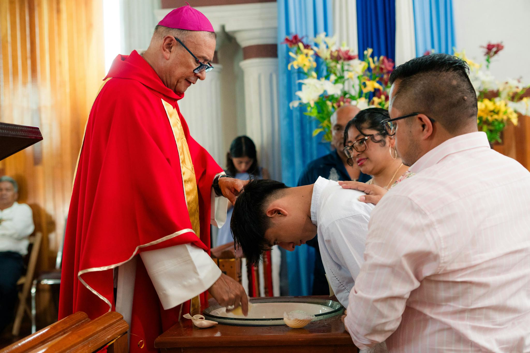 A priest performs a baptism with family gathered in a church setting.