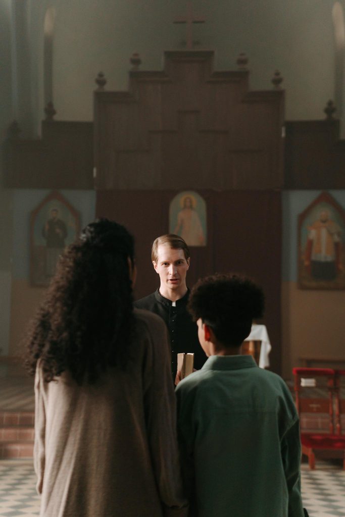 A priest speaking to parishioners inside a church, emphasizing community and faith.